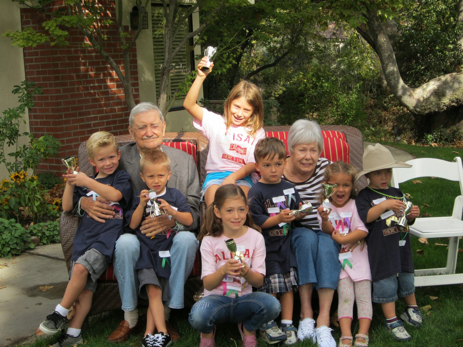 Bonnie and Jerry Thompson seated outdoors, surrounded by their grandchildren holding small trophy cups